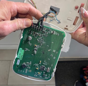 Egy technikus egy riasztórendszer vezérlőpaneljét javítja, amelyen látható a zöld áramköri lap 