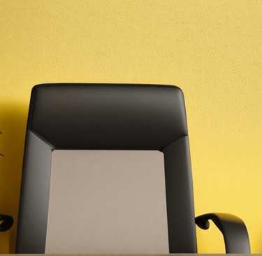 a desk with a chair and a plant in front of a yellow wall