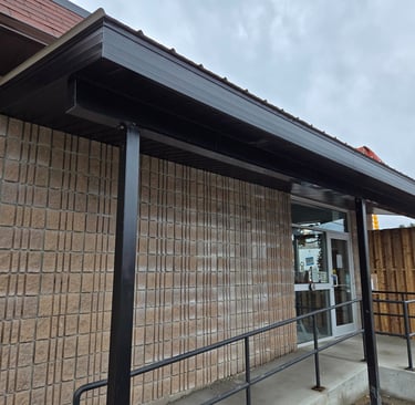 Commercial building exterior featuring a black metal awning, concrete block wall, and accessible entrance ramp.