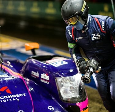 A 24 Hours of Le Mans pit crew member in gear refueling a purple endurance race car during a night pit stop.