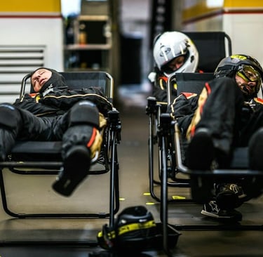 Professional racing pit crew members taking a nap in reclining chairs inside a garage.