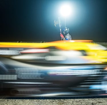 Blurred yellow and black race car speeding past a track official during a night race.