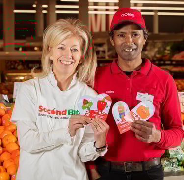a man and woman holding up a sign that says,'Coles SecondBite winter appeal