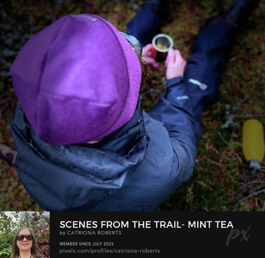 close up photo of a person wearing outdoor clothes sitting on moss holding a mug with liquid in itg