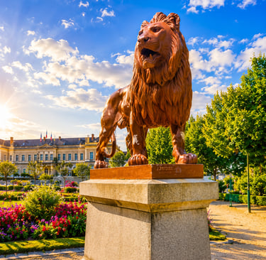 A bronze lion statue by J. Friolet stands in a lush French garden park under a bright blue sky.