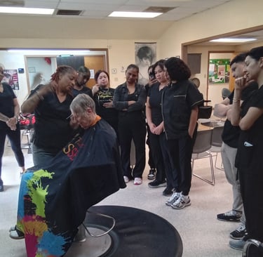 A group of cosmetology students observing a hair cutting demonstration in a salon classroom environment.
