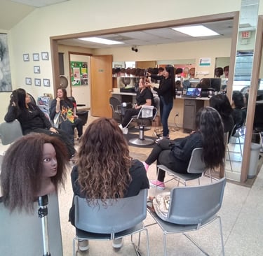 Students in a cosmetology classroom practicing hair styling on mannequins and models.