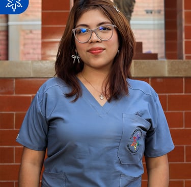 a woman in scrubs and glasses standing in front of a brick wall
