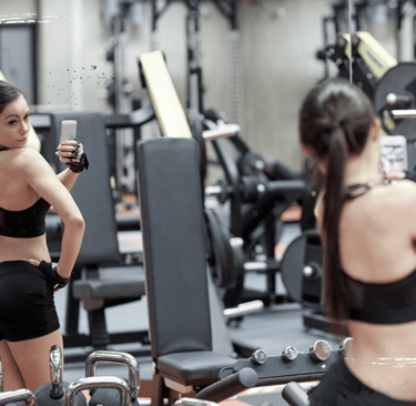 Joven en gimnasio tomándose selfies, reflejo del problema del fitness sin propósito