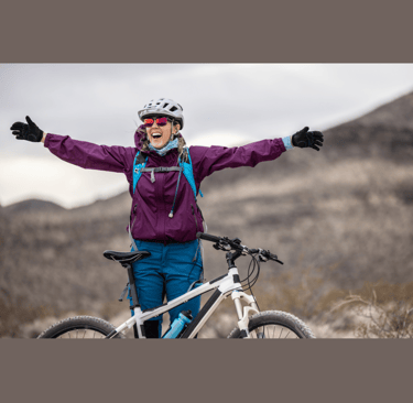 a young woman standing in front of her mountain bike with her arms outstretched 
