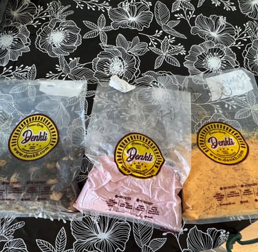 Three bags of Denkli brand organic spice powders and dried goods on a floral tablecloth.