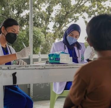 Petugas kesehatan mencatat pemeriksaan pasien di depan puskesmas dalam program pelayanan kesehatan p