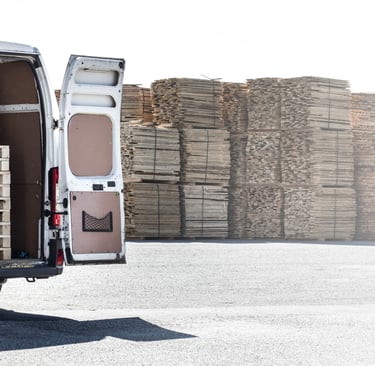 Open van loaded with wooden pallets in an industrial yard, surrounded by stacks of pallets in the background. Represents reli