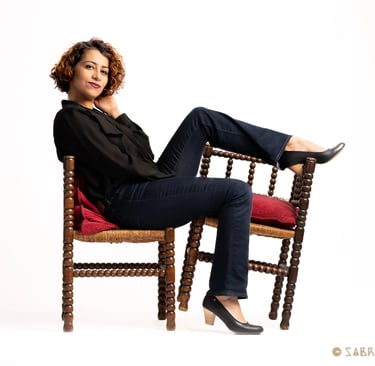 a woman sitting on a chair, pushing a chair with her leg