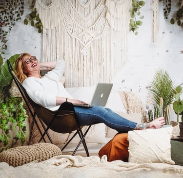 a tattooed corporate woman laughing sitting in a chair with a laptop