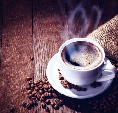 Coffee beans and a steaming cup on a rustic wooden table