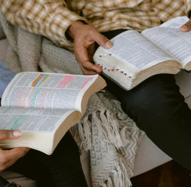 two people sitting and reading a bible in hand
