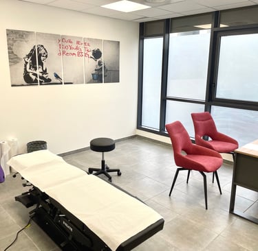 Modern medical consultation room with examination table, red chairs, and Banksy wall art.