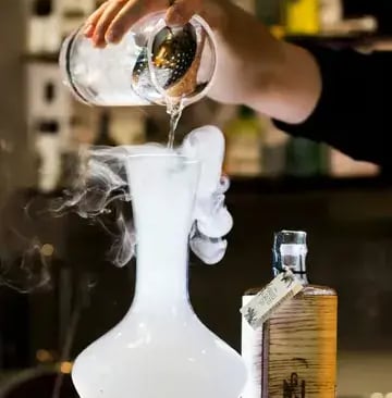 a person pouring a drink into a glass vase
