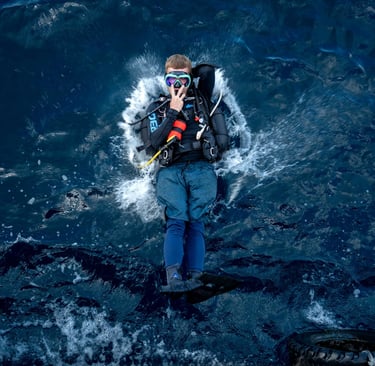 Scuba diver performing a back roll entry into deep blue ocean water from a dive boat.