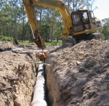 Yellow excavator digging a deep trench for underground pipe installation