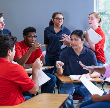 Diverse high school students engage in a group discussion with their teacher in a classroom setting.