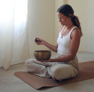 Chica sosteniendo un cuando tibetano, sentada con las piernas cruzadas. Vestida en tonos neutros.