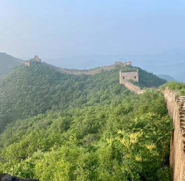 a man standing on a mountain top with a view of the great wall of china