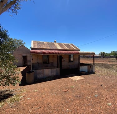 Rustic corrugated iron shack in the Australian outback under a clear blue sky.