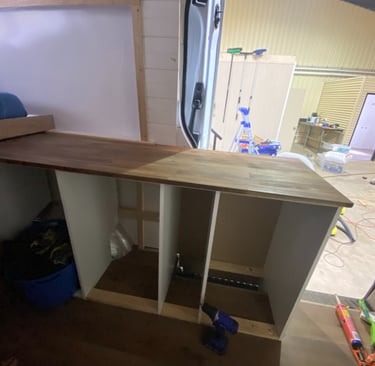 Custom camper van kitchen renovation featuring a wooden butcher block countertop and white cabinets.