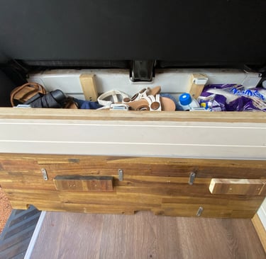 Custom wooden camper van storage bench with sandals and supplies inside a compact living space.