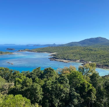 Panoramic view of a tropical island coastline with turquoise coral reefs and lush green mountains.