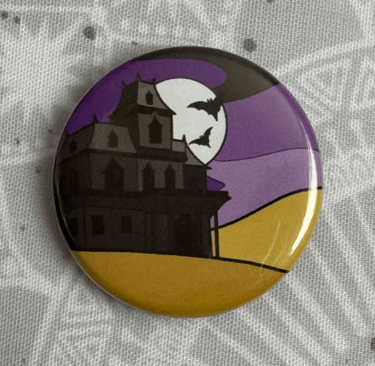 An image of a pin badge with a haunted house illustration in the colours of the non-binary flag.