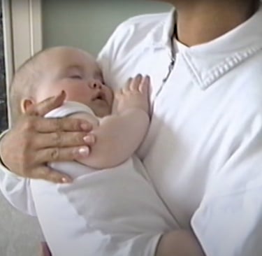 A white baby being rocked and held to the chest of a Filipino woman.