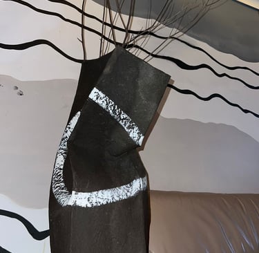 A modern black ceramic vase with abstract white stripes holds dry branches on a rustic wood table.