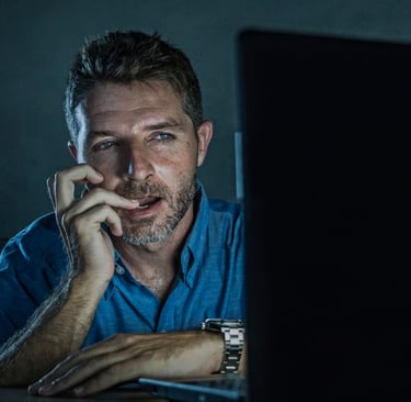 a man sitting at a laptop computer in the dark