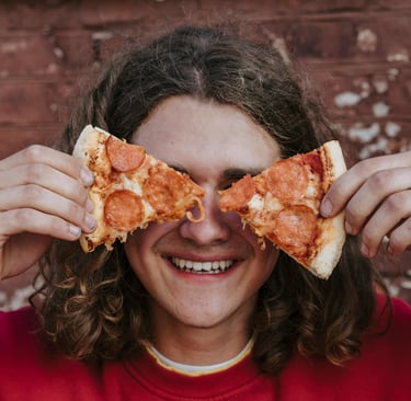 Un adolescent avec des parts de pizza devant ses yeux