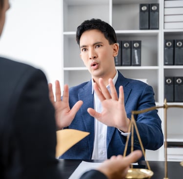 a man in a suit and tie is sitting at a desk hands up