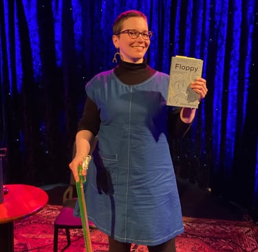 Alyssa Graybeal on stage holding Floppy. Alyssa has buzzed hair, a lime green cane, and glasses.