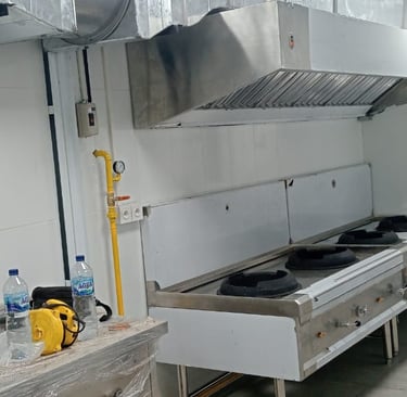 Professional commercial kitchen with stainless steel gas wok ranges and industrial exhaust hood ventilation.