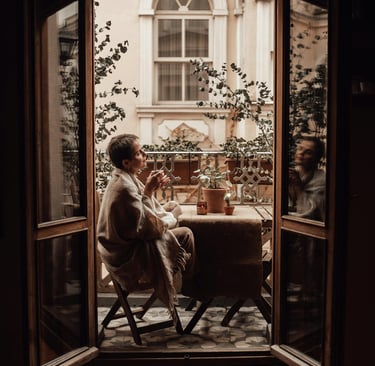 Woman wrapped in a blanket sitting at a cozy outdoor table with tea, enjoying a quiet moment.