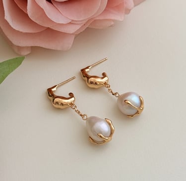 ein natürlicher Perlenohrring, der wie eine Rosenblüte aussieht, und eine Rose auf einem weißen Tisc