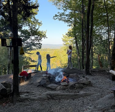 a group of children playing charades around a campfire with New Hampshire mountains beyond
