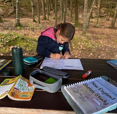 a young child is writing in a journal while road schooling at a picnic table at our campsite