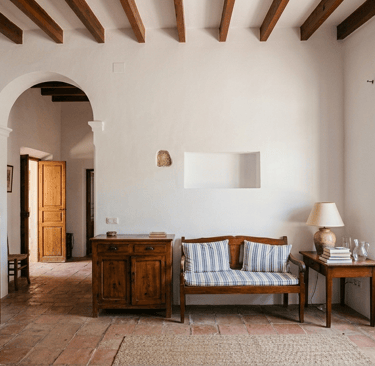 Rustic Mediterranean living room with terracotta tile floors, wooden ceiling beams, and a striped bench.