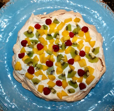 pavlova decorated with kiwi, raspberries and mango