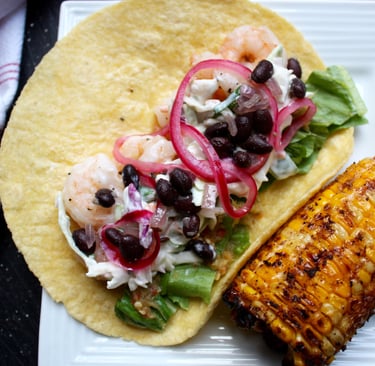 shrimp taco with beans, pickled onions and creamy coleslaw with a side of Mexican corn