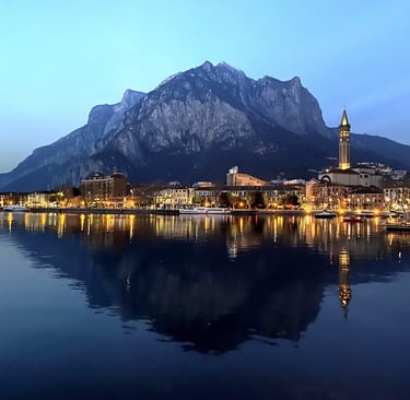 Night view of Lecco on Lake Como, with city lights reflecting on the water and mountain backdrop