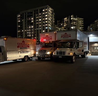 Canada’s Most Wanted Movers fleet parked at night in downtown Vancouver near residential high-rises.