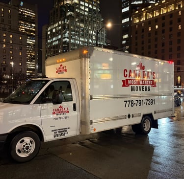 Canada’s Most Wanted Movers box truck operating in downtown Vancouver on a rainy evening.